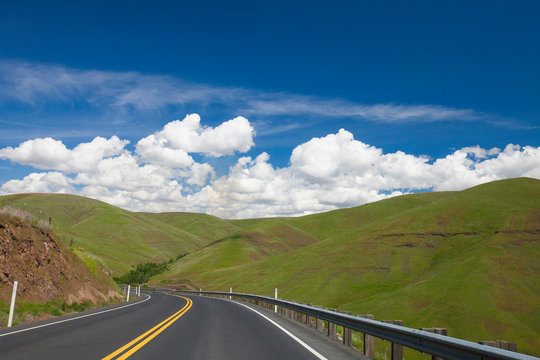 Scenery of country road and green rolling hills under blue sky with clouds, Palouse, Washington State, USA