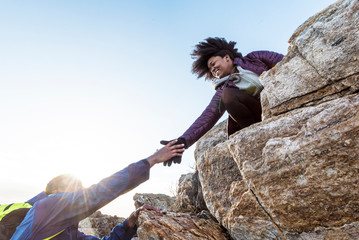 Woman helping man up rock outcrop, Kittery, Maine, USA