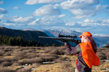 Female hunter aiming with rifle in landscape