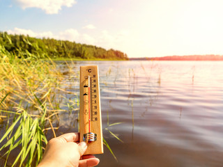 Thermometer showing 30 degrees Celsius of heat against the background of the lake water and the...