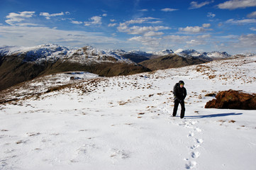 A female hiker climbing in a snowed steep slope with a mountain landscape bacground at The Loch Lomond & The Trossachs National Park, Scotland, UK.