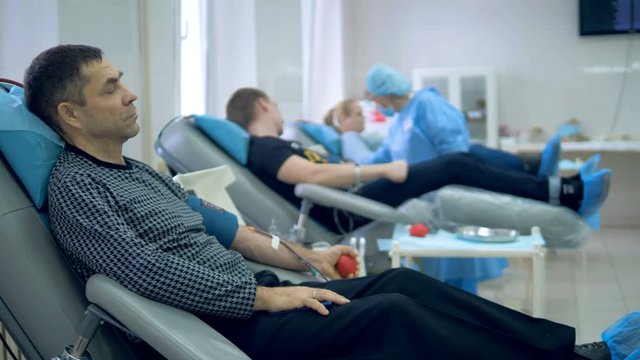 Blood donors sit in chairs, pumping blood in hands.