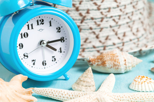 Seashells, alarm clock and beach accessories on a blue table - summer vacation and vacation time concept