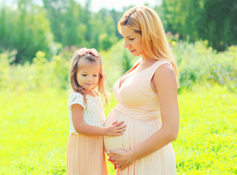 Pregnancy and family concept - happy pregnant woman, little child daughter touches belly mother in summer day