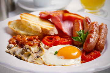 English or Irish breakfast in white plate with sausages, bacon, eggs, tomatoes, mushrooms, toasts and beans. horizontal