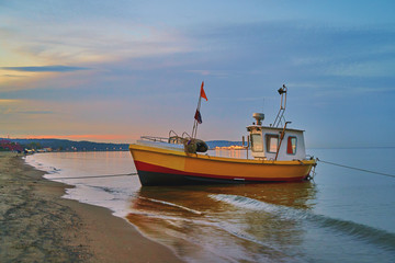 Picturesque landscape of a sunset with a fishing boat on beach in Sopot, Poland.