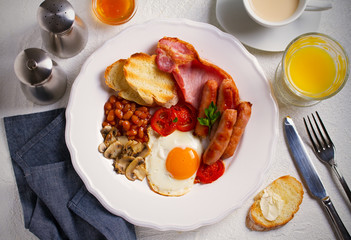 English or Irish breakfast in white plate with sausages, bacon, eggs, tomatoes, mushrooms, toasts and beans. horizontal, overhead