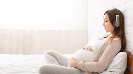 Happy young pregnant woman listening to music in headphones