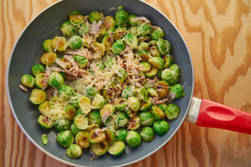 Top view on the frying pan with fresh quickly roasted juicy brussels sprout with ham and cheese and butter, simple, healthy and light vegetable tasty dish, full of nutritions and vitamins for diet.