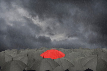 One red umbrella surrounded by black umbrellas in the rain
