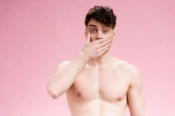 handsome, surprised brunette man covering mouth with hand on pink