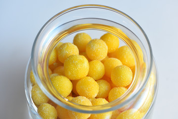 Beautiful fresh yellow sugar dragees are stored in a glass transparent jar on the white background. Close-up