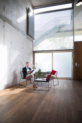 Businessman sitting in a loft at concrete wall reading book