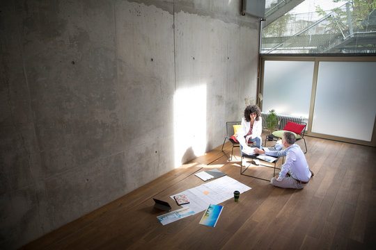 Businessman and businesswoman talking in a loft with documents on the floor