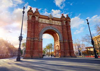 Fototapeta na wymiar Sunrise at Triumphal Arch in Barcelona, Catalonia, Spain. Arc de Triomf at boulevard street. Alley with tropical palm trees. Early morning landscape with shadows and blue sky with clouds. Famous.