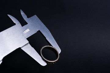 Vintage steel caliper measuring diameter of sterling silver male ring closeup. Ring in focus. Tool...