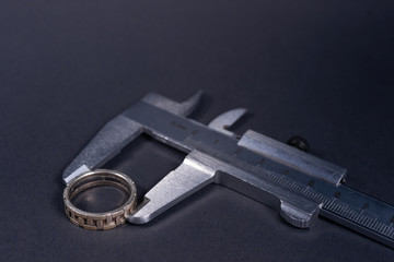 Vintage steel caliper measuring sterling silver male ring closeup. Ring in focus. Tool in very good condition. Stock photo on blurred gray background.