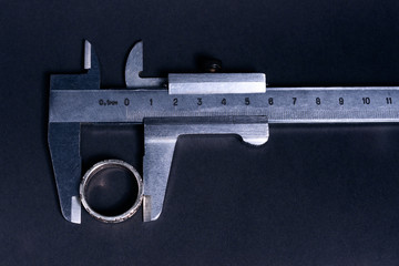 Vintage steel caliper measuring sterling silver male ring closeup. Scale and ring in focus. Tool in...