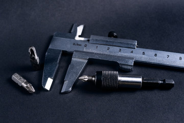 Vintage steel caliper with modern tool bits and bitholder on dark background. Caliper and bitholder in focus. Tools in very good condition. Stock photo on blurred dark gray background.