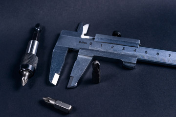 Vintage steel caliper with modern tool bits and bitholder on dark background. Caliper and bitholder in focus. Tools in very good condition. Stock photo on blurred dark gray background.
