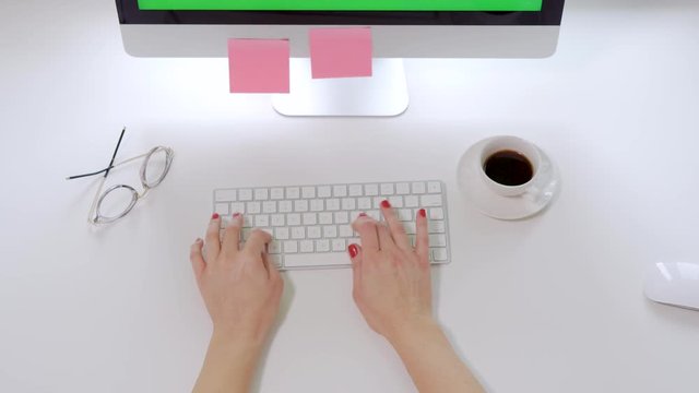 Top view on the white office desk with coffe and computer keyboard and female hands with red nails typing on it