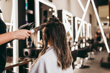 Beautiful brunette woman with long hair at the beauty salon getting a hair blowing. Hair salon styling concept.