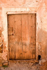 close up of an old wooden closed door in a wall of concrete, mud and stone in a closed abandoned house where nobody lives. Vertical photo.