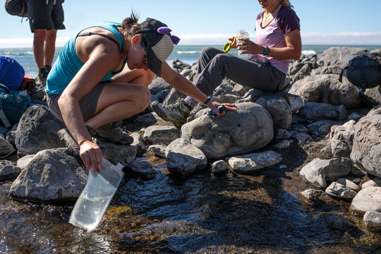 Female hiker refilling water bladder from stream, Lost Coast Trail, Kings Range National Conservation Area, California, USA