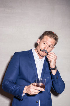 Portrait of young man with drink and fake moustache at a party