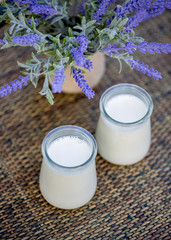 Homemade milk sweet yogurt. Dessert. Milk yogurt in glass jars on wooden table in summertime. Lavender flowers. Summer twilight. Soft focus. Blurry background. Close-up. Copy space. Top view.