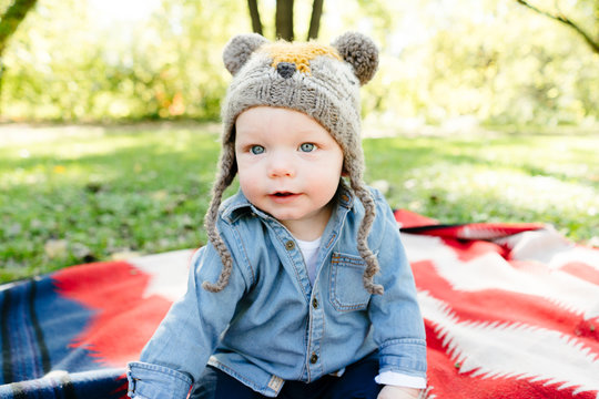 A child in a hat sits on a blanket outside