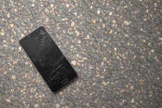 smartphone with a crashed and dirty screen on asphalt