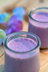 Homemade milk sweet yogurt with bilberry. Blueberry yogurt in glass jars on wooden table in summertime. Dessert. Color lavender. Evening light. Soft focus. Blurry background. Close-up. Macro. Top view