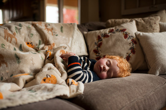 young boy sleeping on couch at home under warm blanket