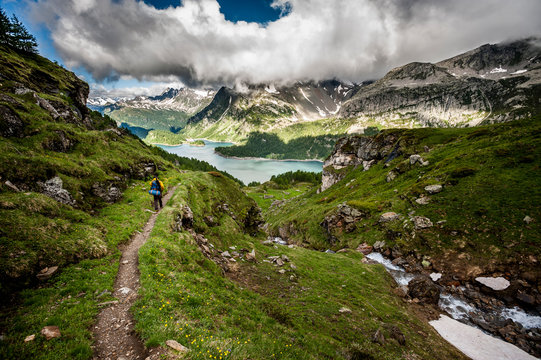 Man hiking at sunrise in Devero National Park, with a view of Devero's Lake and the Lepontine Alps. Ossola, Italy.