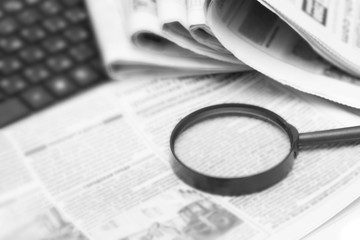 Newspapers, magnifier and laptop. A pile of daily newspapers with news Headlines. Modern gadgets and old magazines.