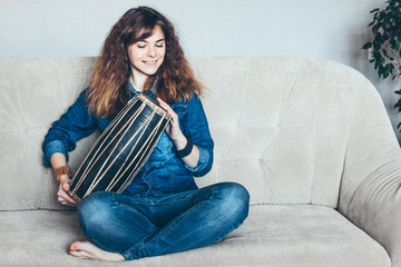 Obraz premium Young woman playing ethnic indian hand drum mridangam at home.
