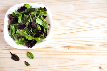 Plate with lettuce on a wooden background. Salad greens. Organic food. Food For Vegans. Design a banner with natural food. Salad to lose weight. Flat lay, top view.