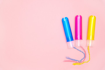 three cotton tampons with blue pink yellow applicartors on pink background. Menstrual cycle period concept. Woman days hygiene protection. Top view, flat lay