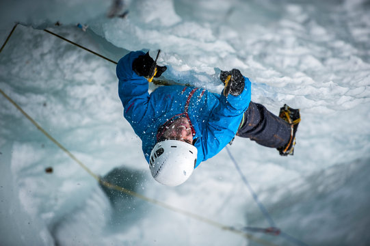 Man with blue   jacket lead climbing an ice fall in the middle of a snow storm in Simplon Pass shooted from above. Valais, Switzerland.