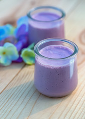 Blueberry yogurt in glass jars on wooden table in summertime. Homemade milk sweet yogurt with bilberry. Dessert. Color lavender. Evening light. Soft focus. Blurry background. Close-up. Copy cpace.