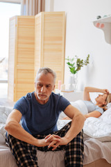 Mature man wearing pajamas feeling concerned sitting near wife