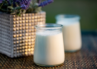 Milk yogurt in glass jars on rustic table in summertime. Homemade milk sweet yogurt. Dessert. Lavender flowers. Evening light. Soft focus. Blurry background. Close-up. Macro. Copy space.