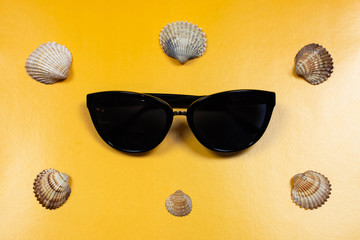 Flat lay na żółtym tle, okulary przeciwsłoneczne i muszelki. Inspiracja na wakacje, lato, czas wolny - obrazy, fototapety, plakaty