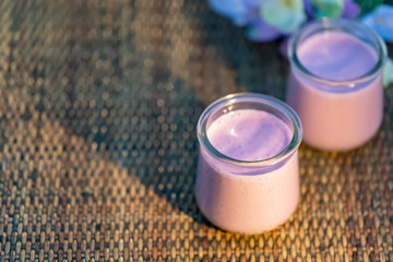 Blueberry yogurt in glass jars on rustic table in summertime. Homemade milk sweet yogurt with bilberry. Evening light. Soft focus. Blurry background. Close-up. Copy cpace. Top view.