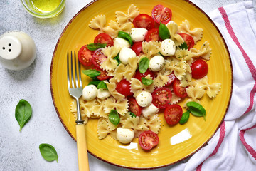 Traditional italian pasta caprese : farfalle, mozzarella balls, cherry tomato and basil. Top view with copy space.