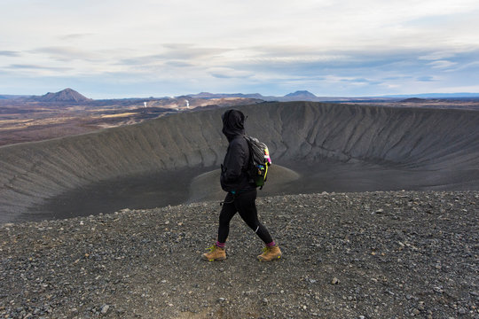 Young woman walking along the ridge of the Hverfjall crater with looking at the volcanic landscape in the background in the background.
