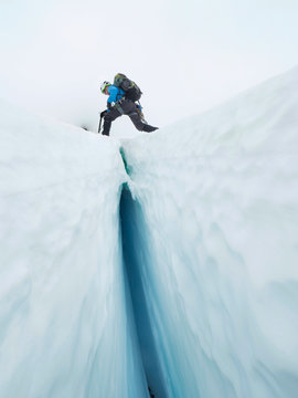 Climber Steps Over Crevasse In Glacier