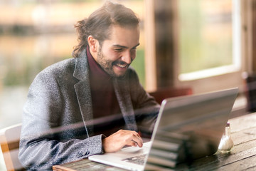 Smiling man using laptop at table in cafe