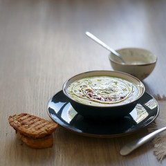Creamy vegetable soup with kale, cabbage, celery and millet, decorated with olive oil, yoghurt sauce and chilli flakes. Served with toasted bread and lemony yoghurt sauce. Selective focus.
